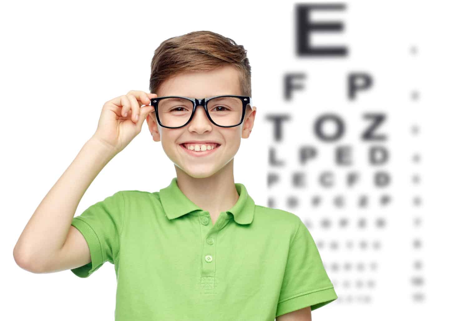 childhood, vision, eyesight and people concept - happy smiling boy in green polo t-shirt in eyeglasses over eye chart background