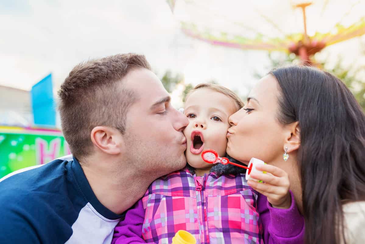 Father, mother kissing their daughter blowing bubbles, amusement