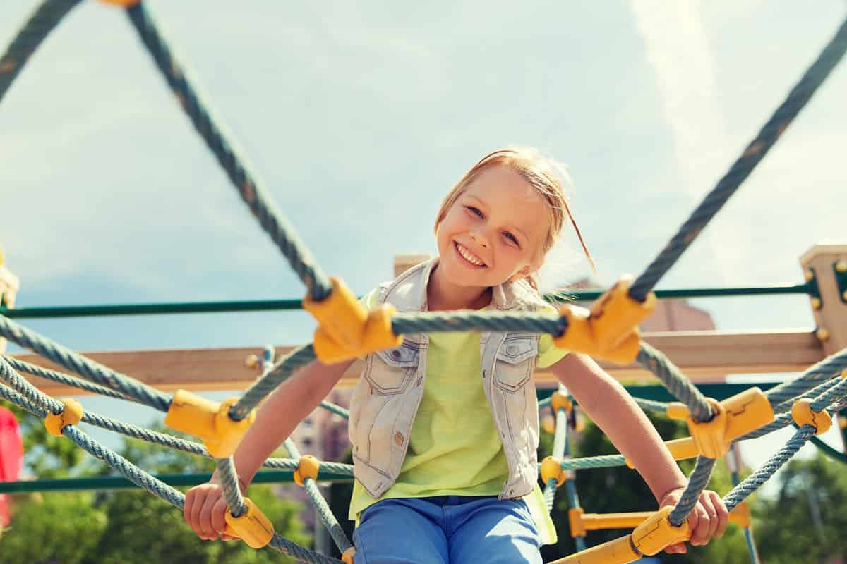 summer, childhood, leisure and people concept - happy little girl on children playground climbing frame