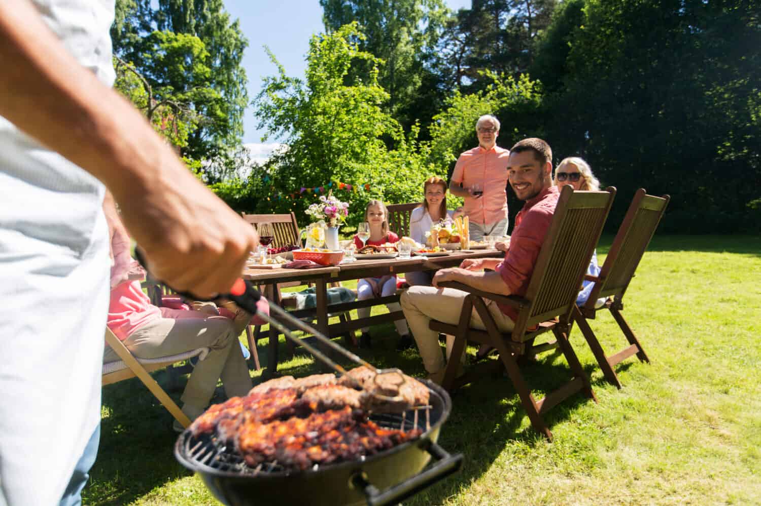 food, people and family time concept - man cooking meat on barbecue grill at summer garden party