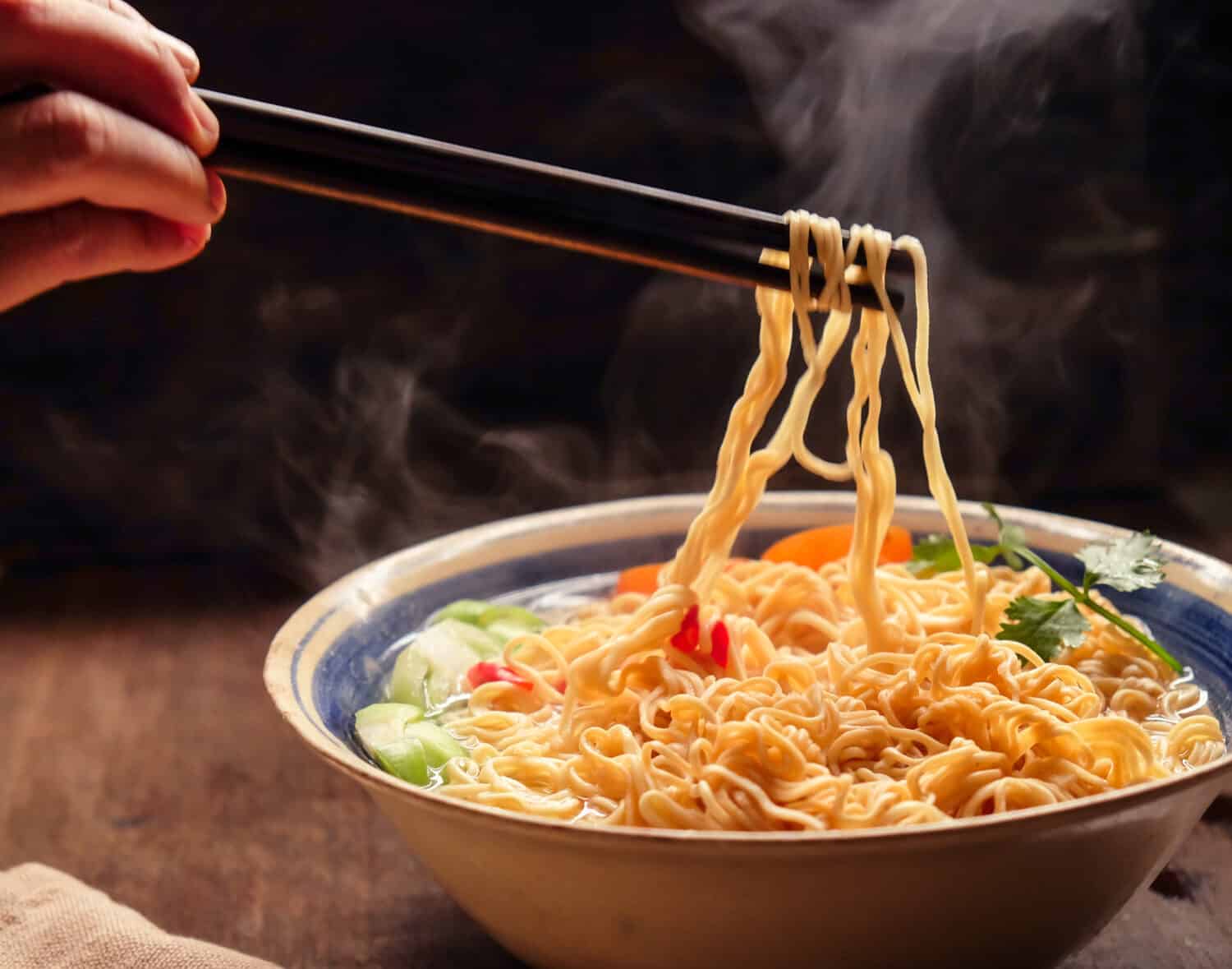 Hand uses chopsticks to pickup tasty noodles with smokes.