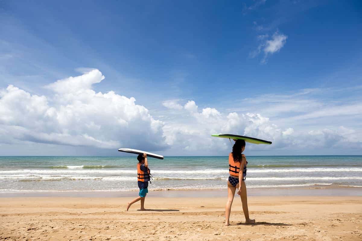 Young boy and girl with surfing boards walking on tropical ocean beach