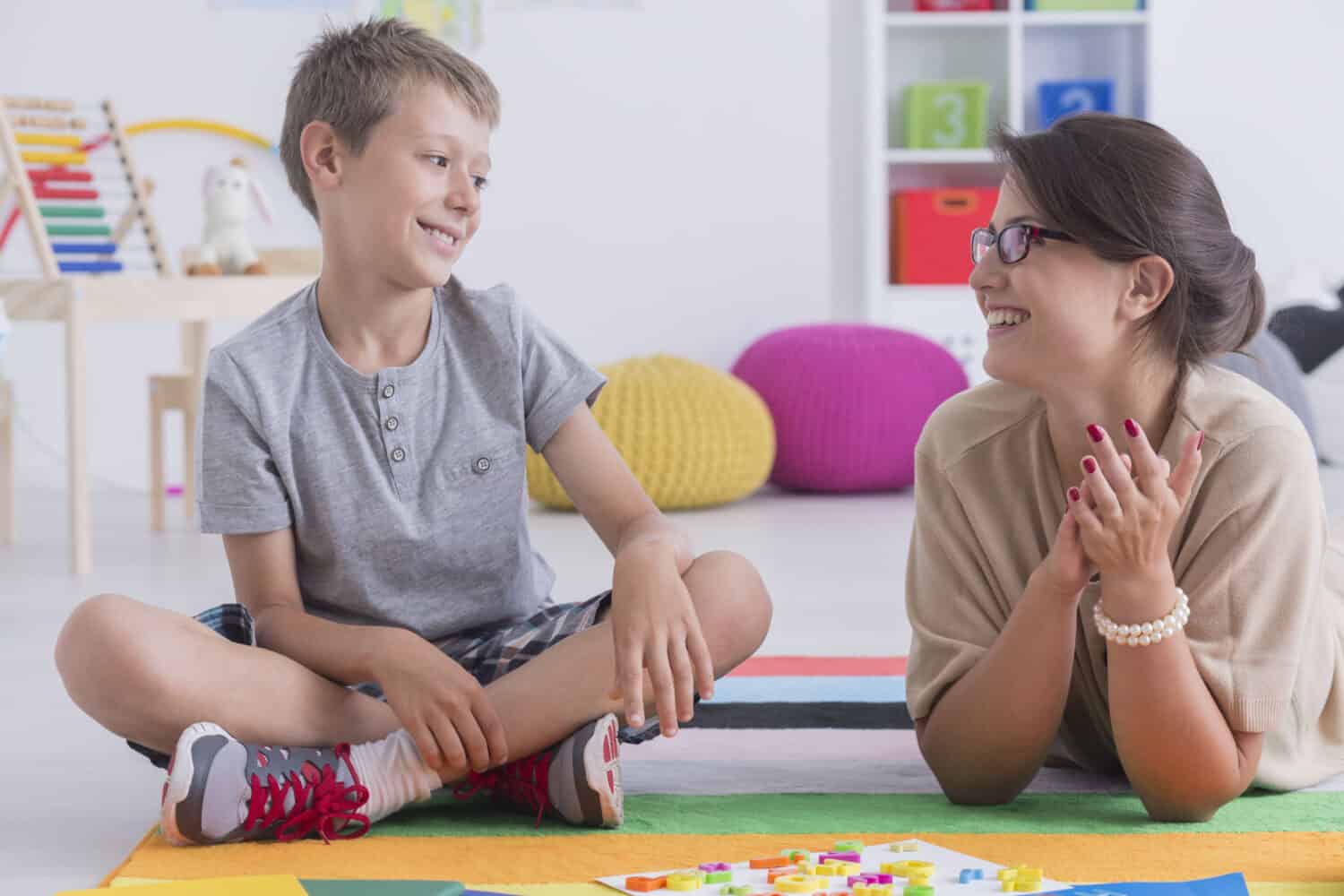 Happy little child during during therapy with school counselor, learning and having fun together sitting on the floor in a colorful playroom