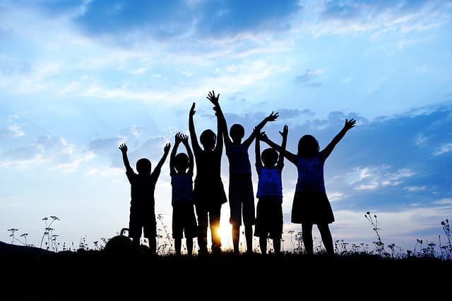 group of happy children playing on meadow, blue sky, summertime