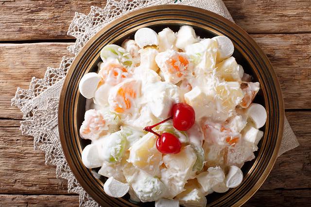 Light fruit salad Ambrosia with marshmallow and vanilla yogurt close-up on a plate.