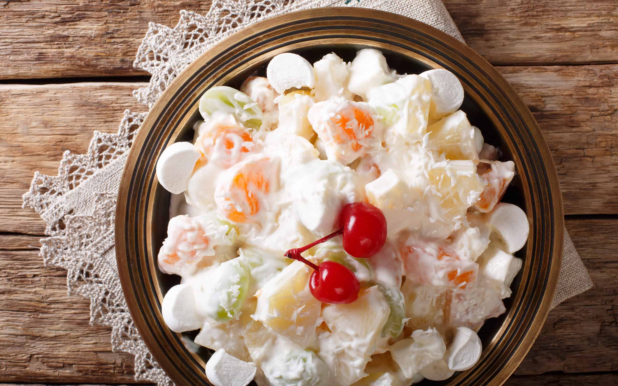 Light fruit salad Ambrosia with marshmallow and vanilla yogurt close-up on a plate.