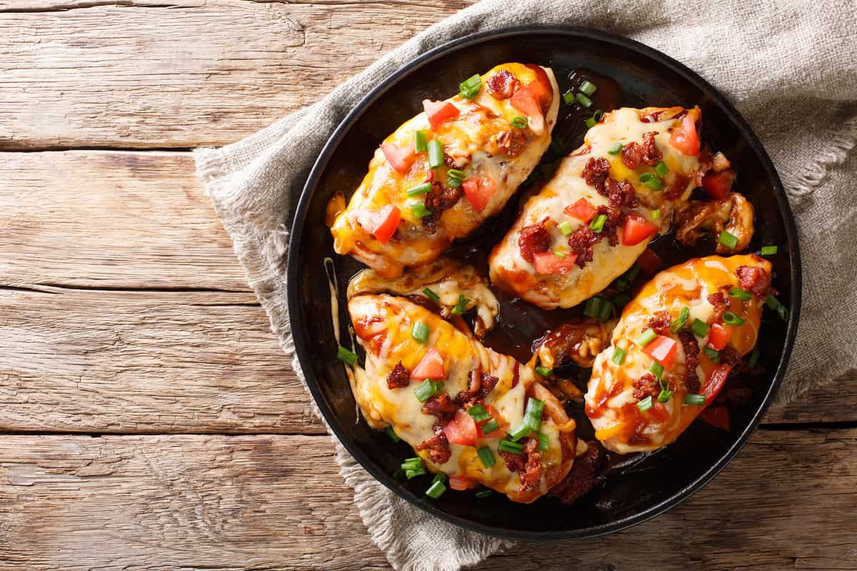 Chicken breast baked with monterey cheese and cheddar, bacon, tomatoes and barbecue sauce close-up on the table. horizontal top view from above