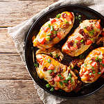 Chicken breast baked with monterey cheese and cheddar, bacon, tomatoes and barbecue sauce close-up on the table. horizontal top view from above