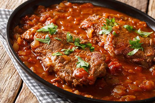 Classic Swiss steak fried and slowly cooked in a fragrant tomato sauce with vegetables close-up on the table