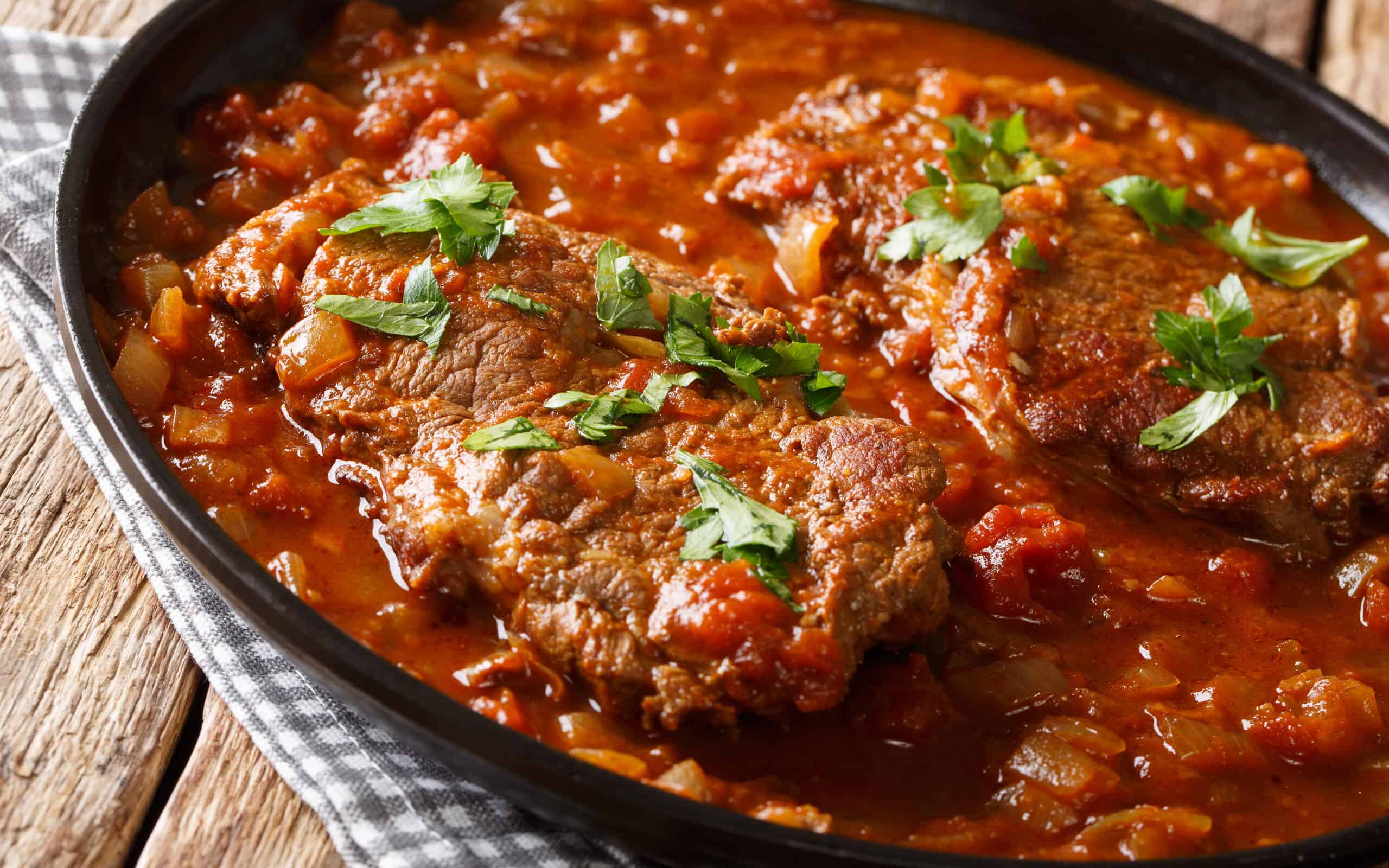 Classic Swiss steak fried and slowly cooked in a fragrant tomato sauce with vegetables close-up on the table