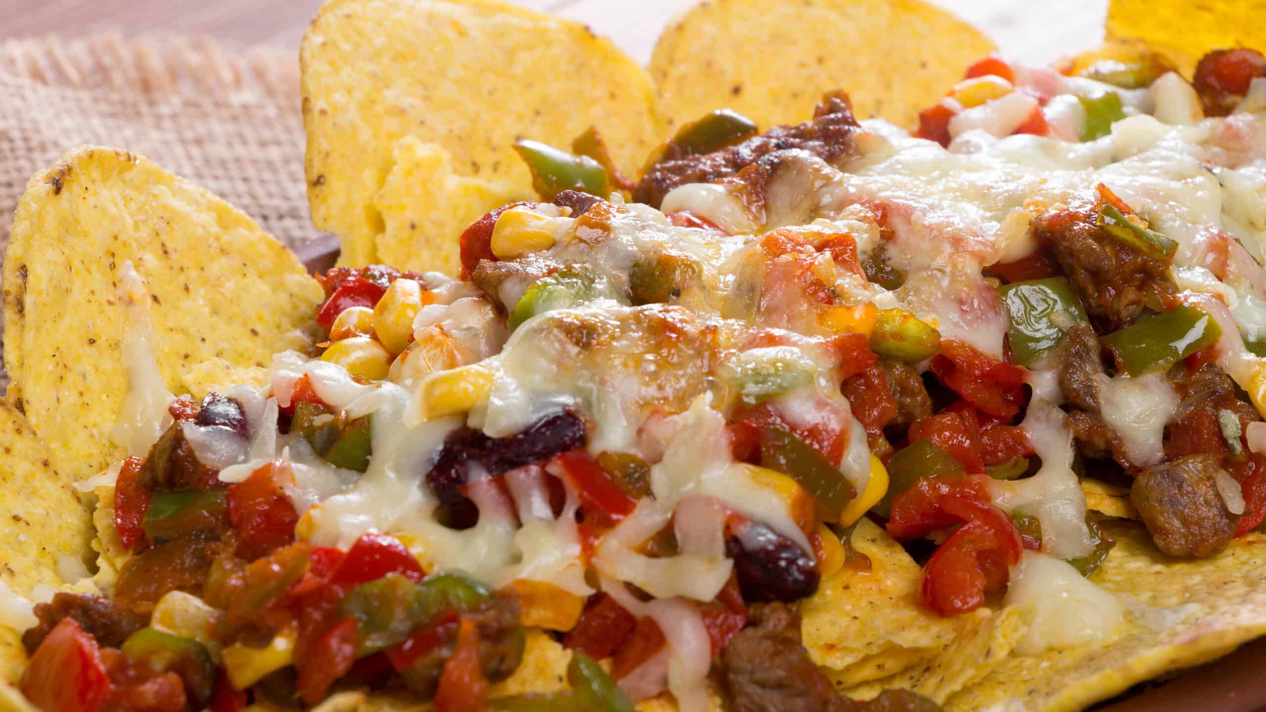 Mexican Nachos baked in a casserole with cheese, beans, corn, hot jalapeno, chicken, red pepper, and mushrooms served on a wooden table.