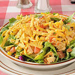 A bowl of taco salad with tortilla strips, corn, tomatoes, chicken and lettuce