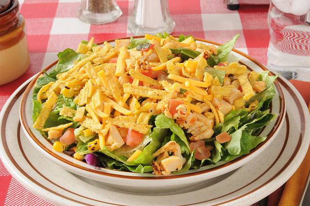 A bowl of taco salad with tortilla strips, corn, tomatoes, chicken and lettuce