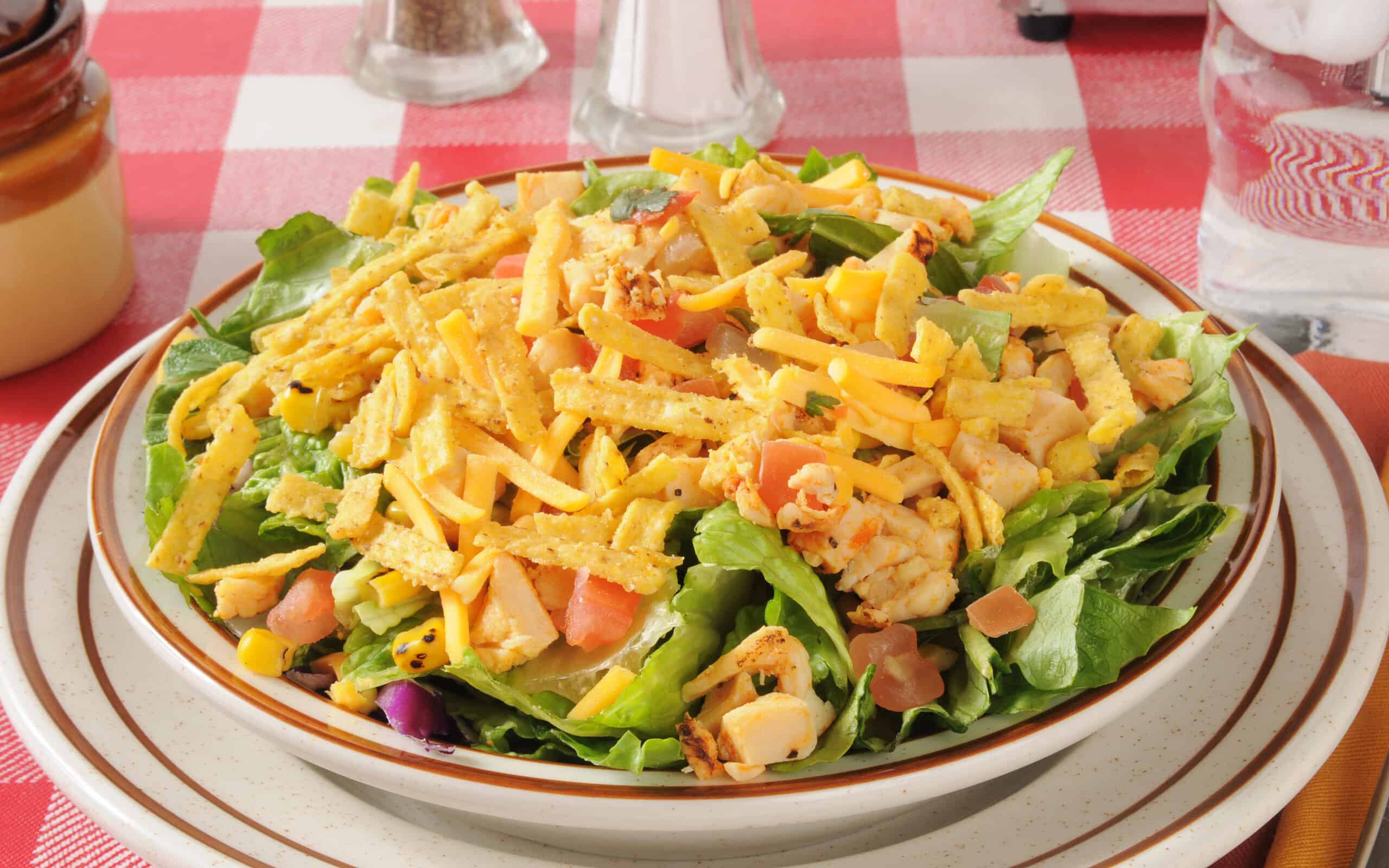 A bowl of taco salad with tortilla strips, corn, tomatoes, chicken and lettuce