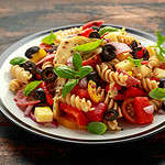 Antipasto salad with pasta, tomato, olives, red onion, bell pepper, salami, cheese artichoke and basil on wooden table