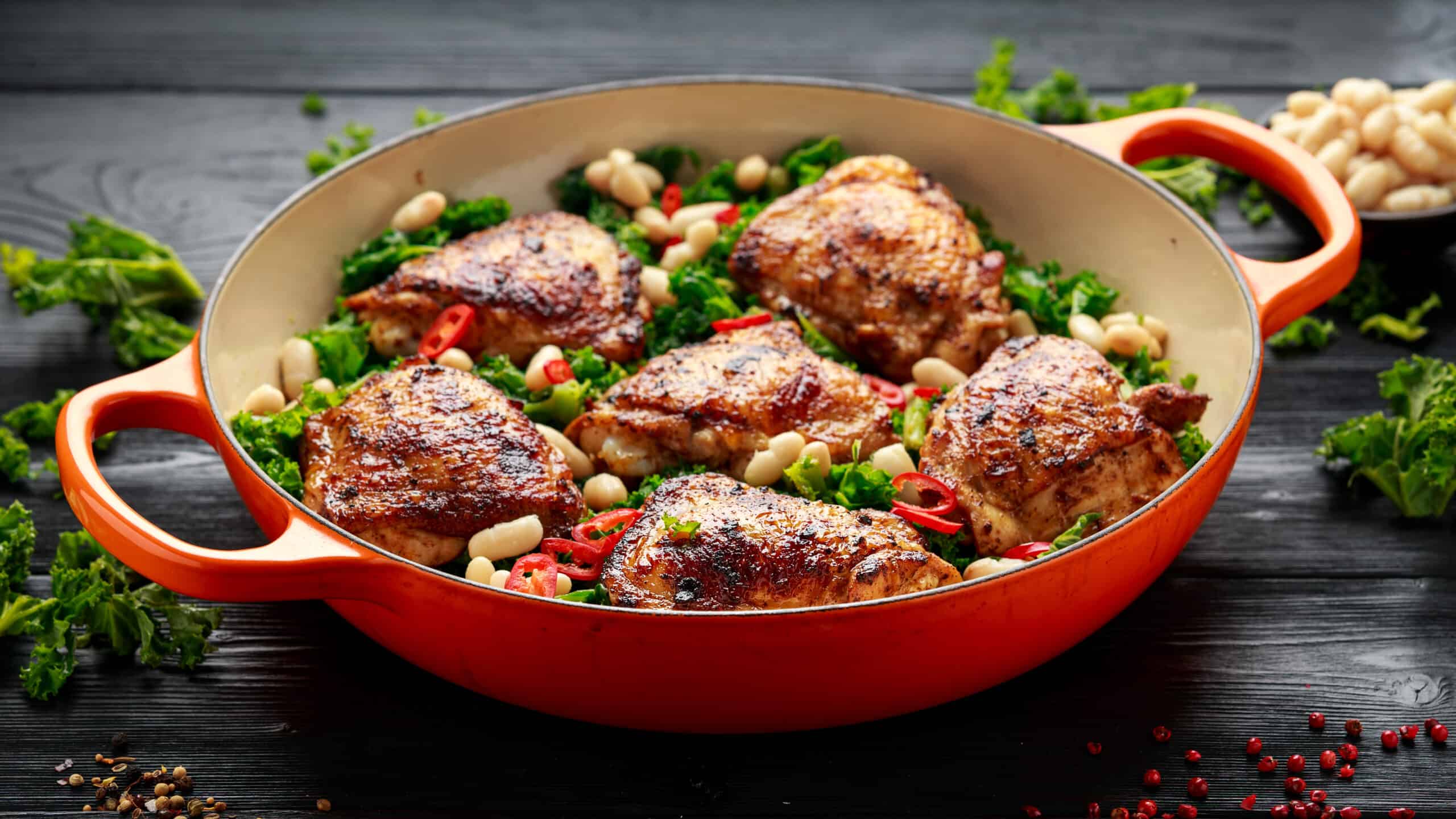 One-pot braised chicken thighs with kale and cannellini beans served with chili peppers