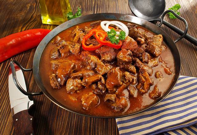 Beef Goulash in a Pan with Red Pepper on wooden Background