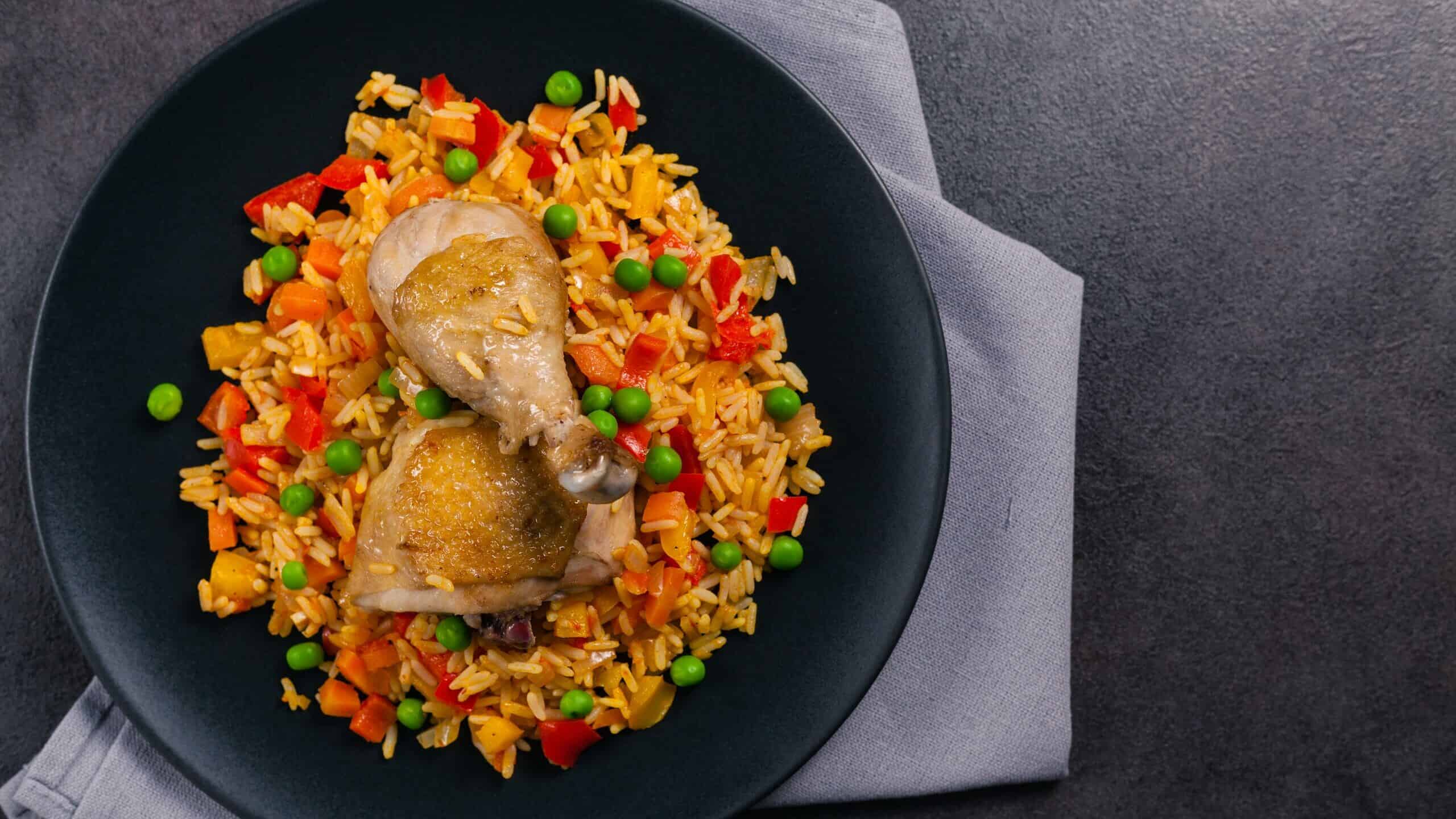 Arroz con pollo. Baked pieces of chicken with bone, rice with paprika and peas. Black background. Served on black plate or spanish pan.