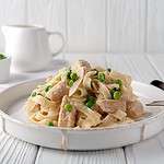 Homemade pasta with green peas, chicken and creamy sauce on a white wooden background