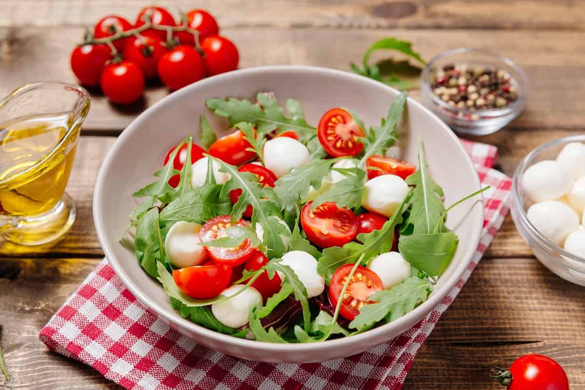 Fresh summer vegetable salad with mozzarella cheese, green arugula leaves and cherry tomatoes on wooden table background.