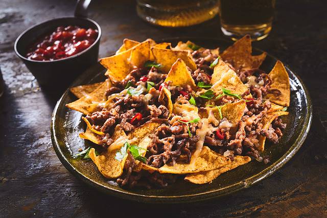 Tortilla chips garnished with ground beef, melted cheese, peppers, and cilantro leaves in a plate on a wooden table