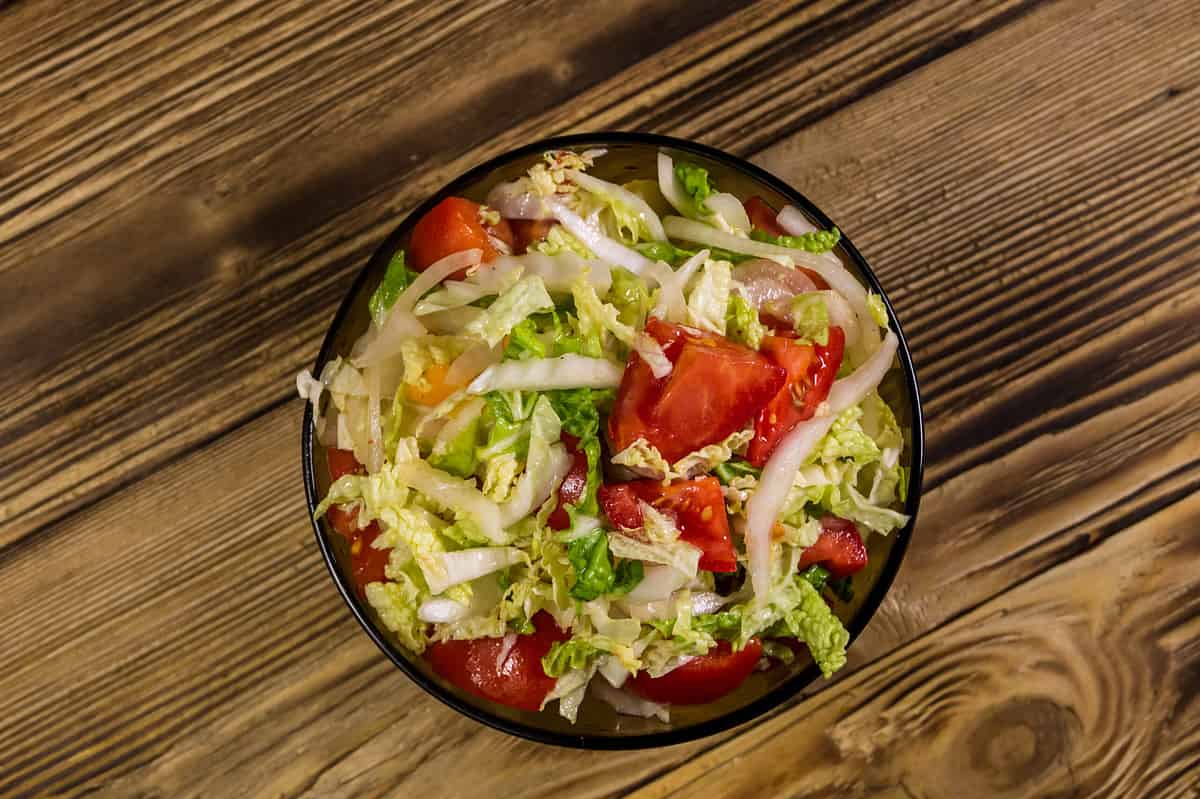 Fresh vegetable salad of chinese cabbage, tomato, pepper and onion with olive or sunflower oil on wooden table