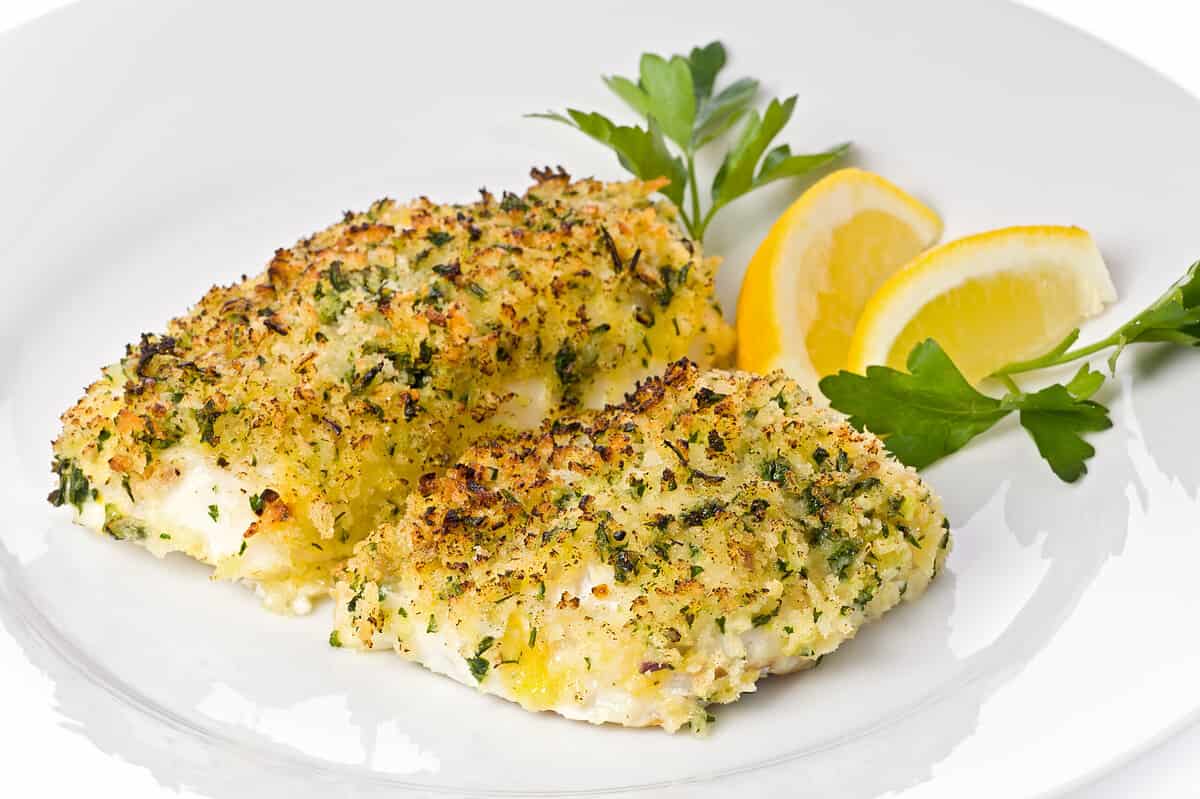 Baked cod with breadcrumbs on a white plate garnished with lemon slices and parsley.