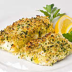 Baked cod with breadcrumbs on a white plate garnished with lemon slices and parsley.