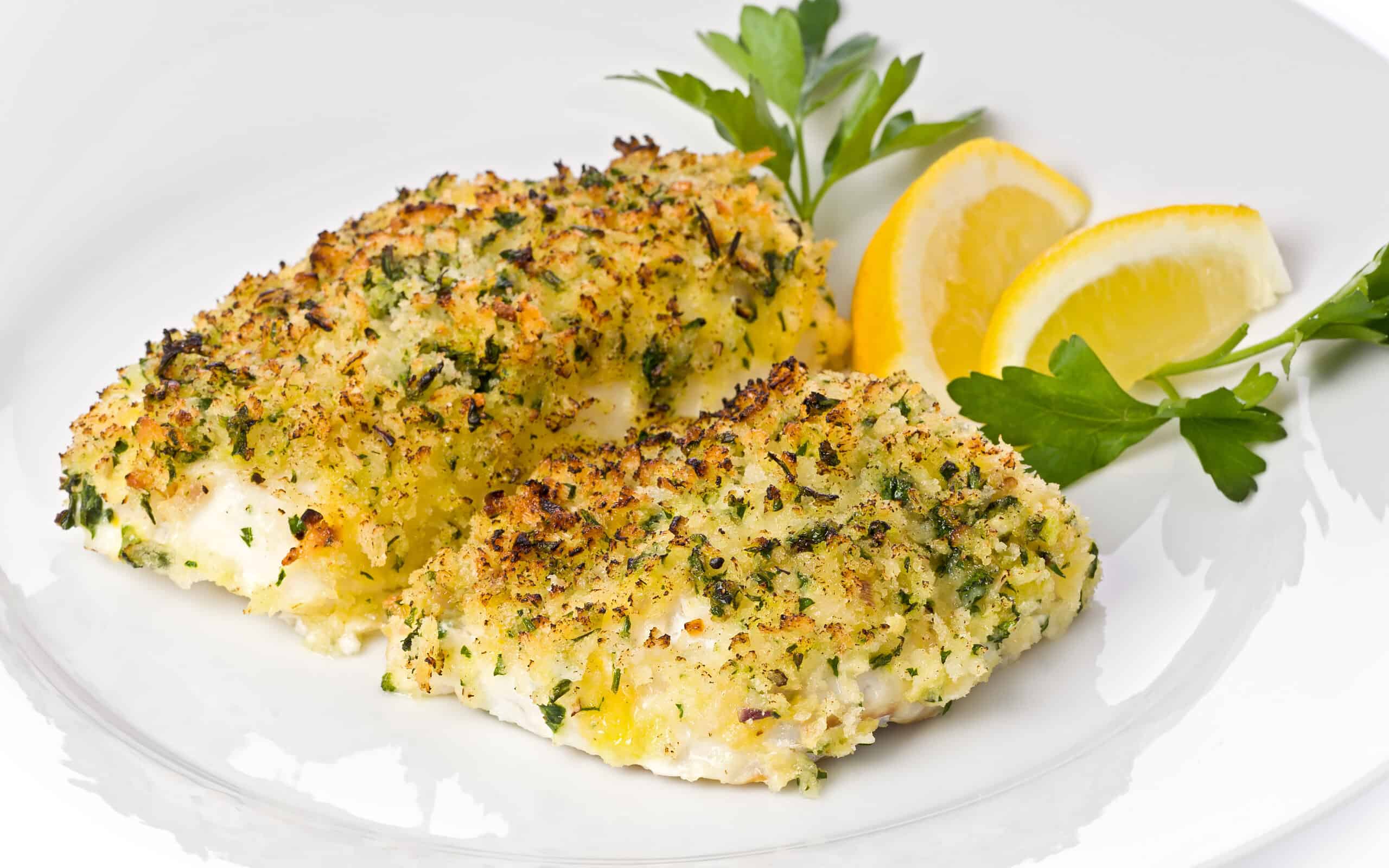 Baked cod with breadcrumbs on a white plate garnished with lemon slices and parsley.