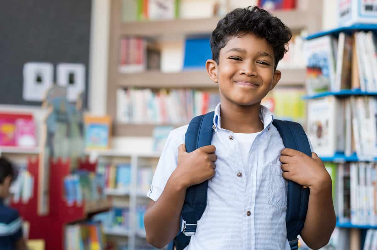 Photo of a young school boy looking at the camera with his backpack on.