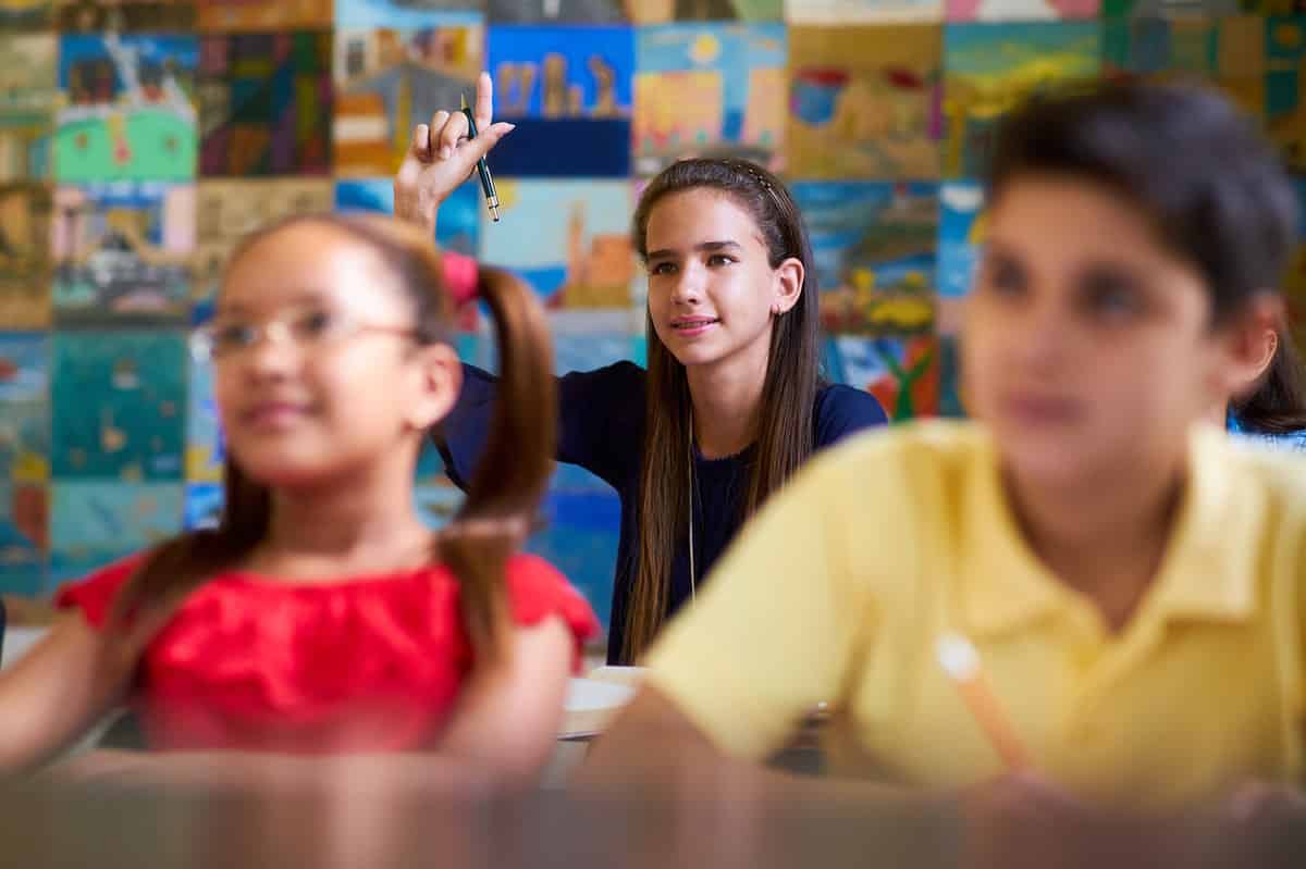 A young girl raising her hand in class. 