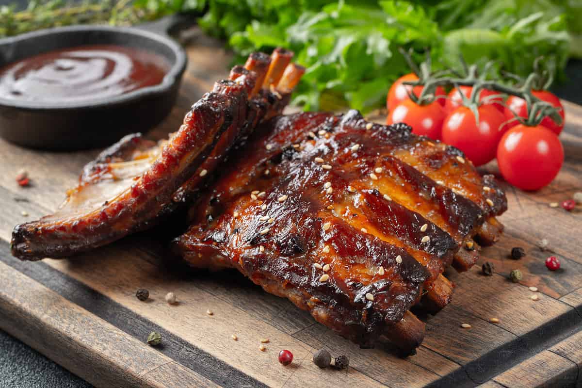 Closeup of pork ribs grilled with BBQ sauce and caramelized in honey. Tasty snack to beer on a wooden Board for filing on dark concrete background.