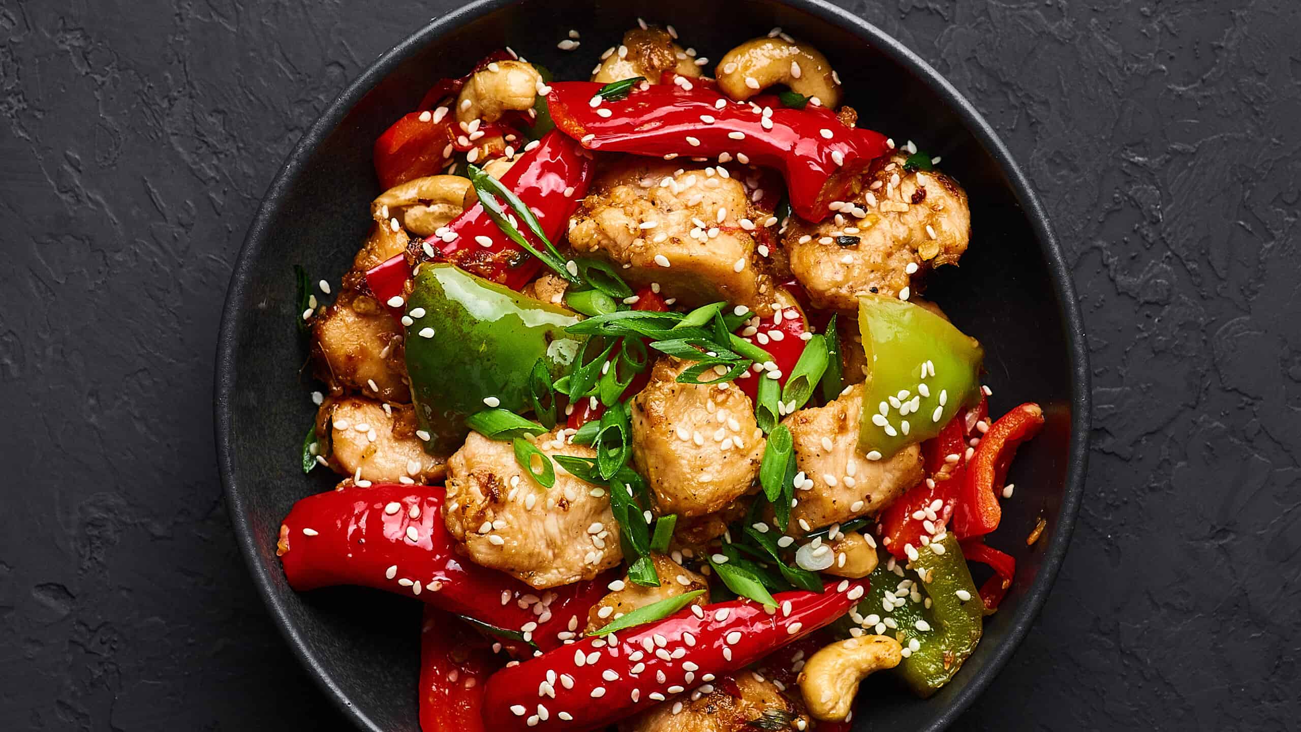 Schezwan Chicken or Dragon Chicken in black bowl at dark slate background. Szechuan Chicken is popular indo-chinese spicy dish with chilli peppers, chicken and vegetables.