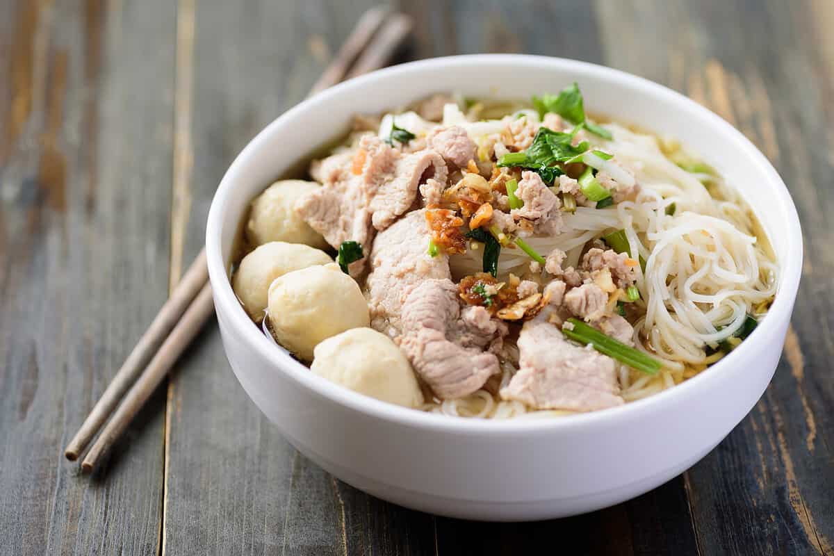 Rice noodles soup with pork and meat ball in a bowl with chopsticks on wooden table, Thai style