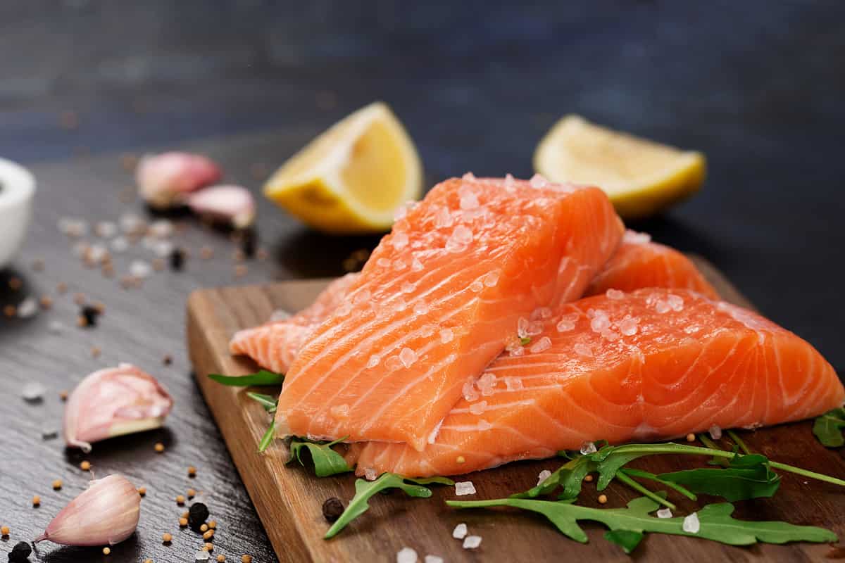 Raw fillet of salmon with sea salt, lemon and pepper on black stone background. Fresh fish prepared for cooking. Top view, copy space. Healthy Brain Food concept.