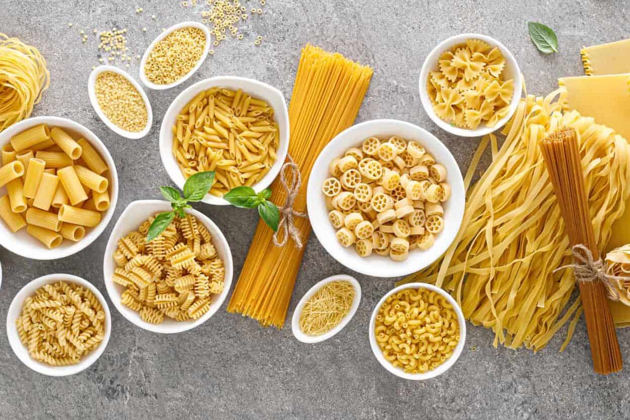 Pasta. Various kinds of uncooked pasta and noodles over stone background, top view with copy space for text. Italian food culinary concept. Collection of different raw pasta on cooking table