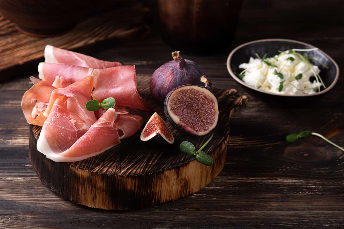 Prosciutto slices with figs on a dark wooden background