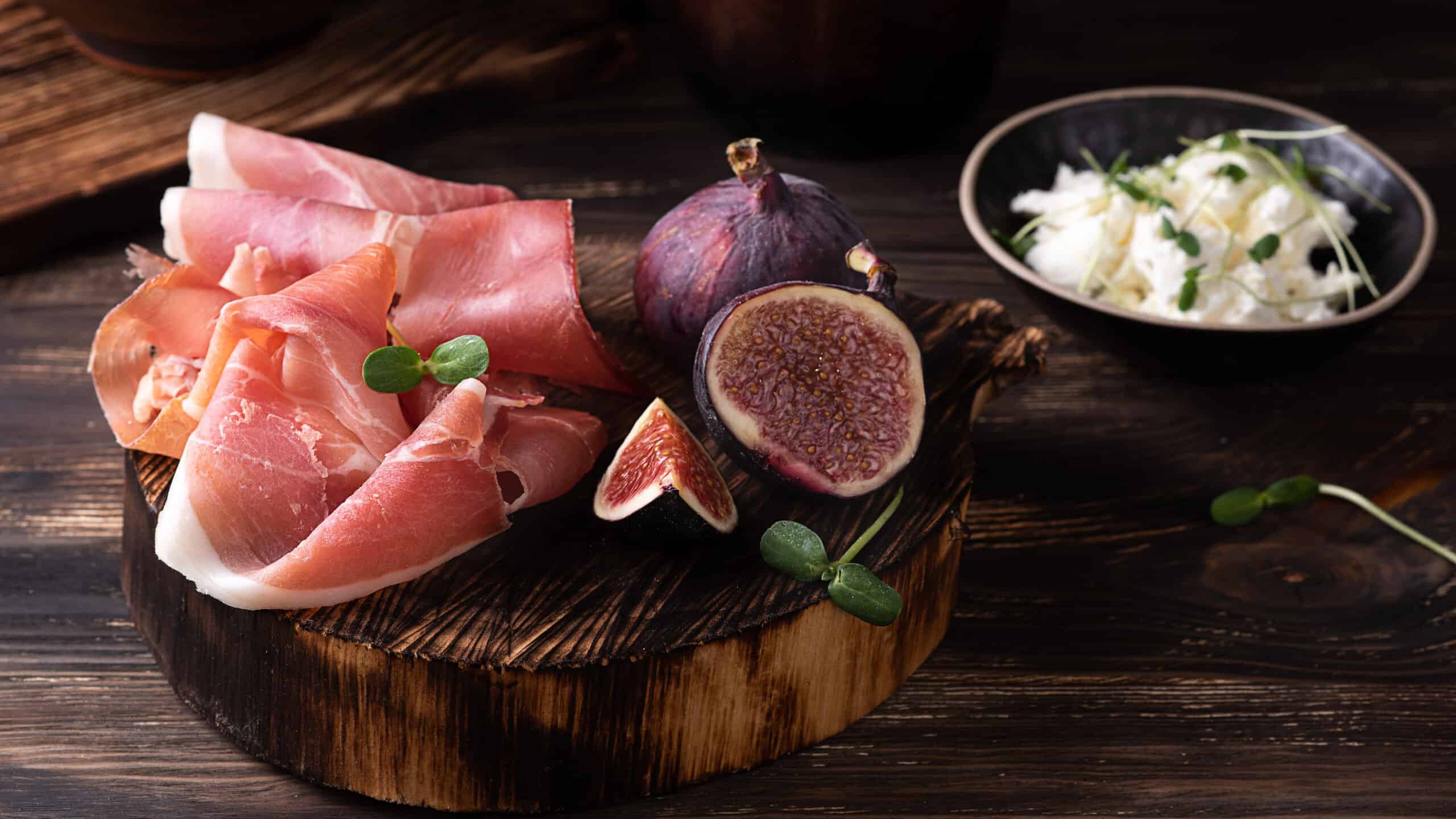 Prosciutto slices with figs on a dark wooden background