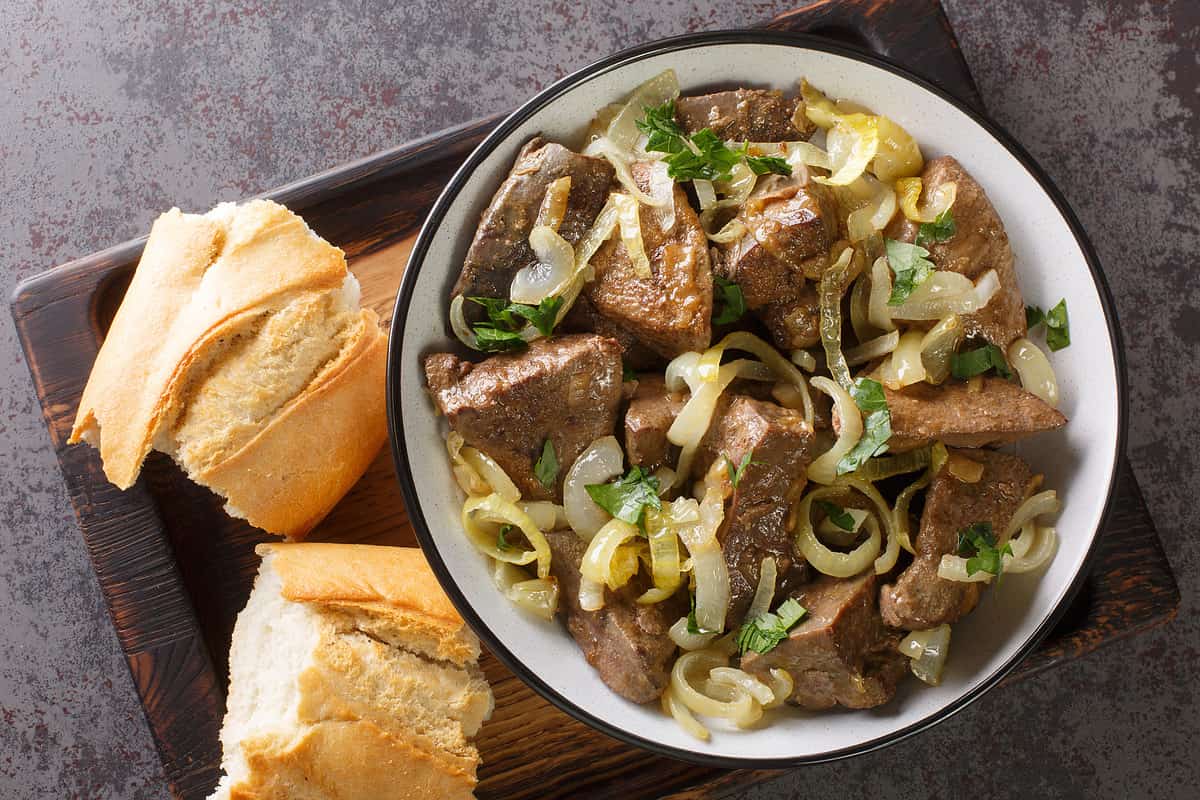 Homemade food fried beef liver with onions and herbs close-up in a plate and bread on a wooden tray on the table. horizontal top view from above