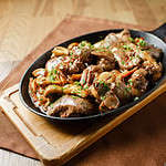 Liver baked with mushrooms, bacon and herbs in a frying pan on a wooden board closeup close lie knife and fork