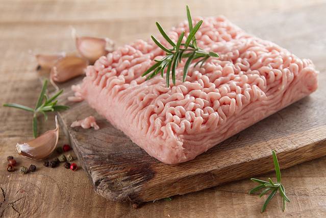 Minced chicken or turkey meat on wooden board with basil and spices, selective focus