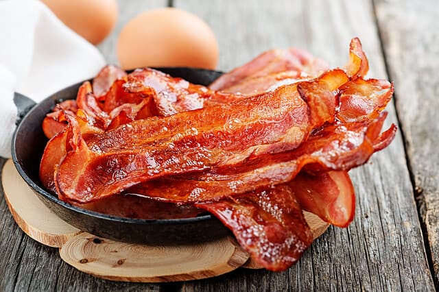 Hot fried bacon pieces in a cast iron skillet.top view