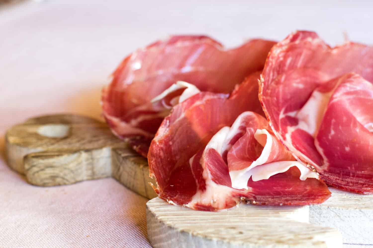 closeup of a chooping wooden board with thin slices of seasoned culatello 