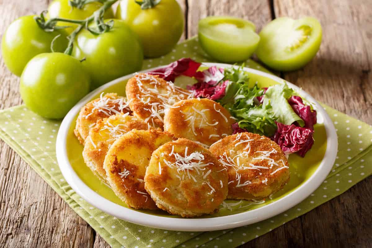 American food: fried green tomatoes with fresh salad close-up on a plate and ingredients on a table. horizontal