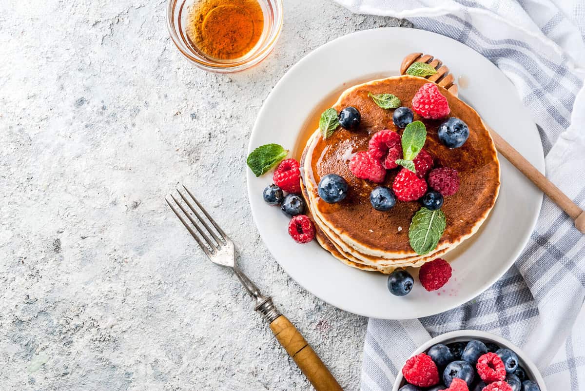 Healthy summer breakfast,homemade classic american pancakes with fresh berry and honey, morning light grey stone background copy space top view