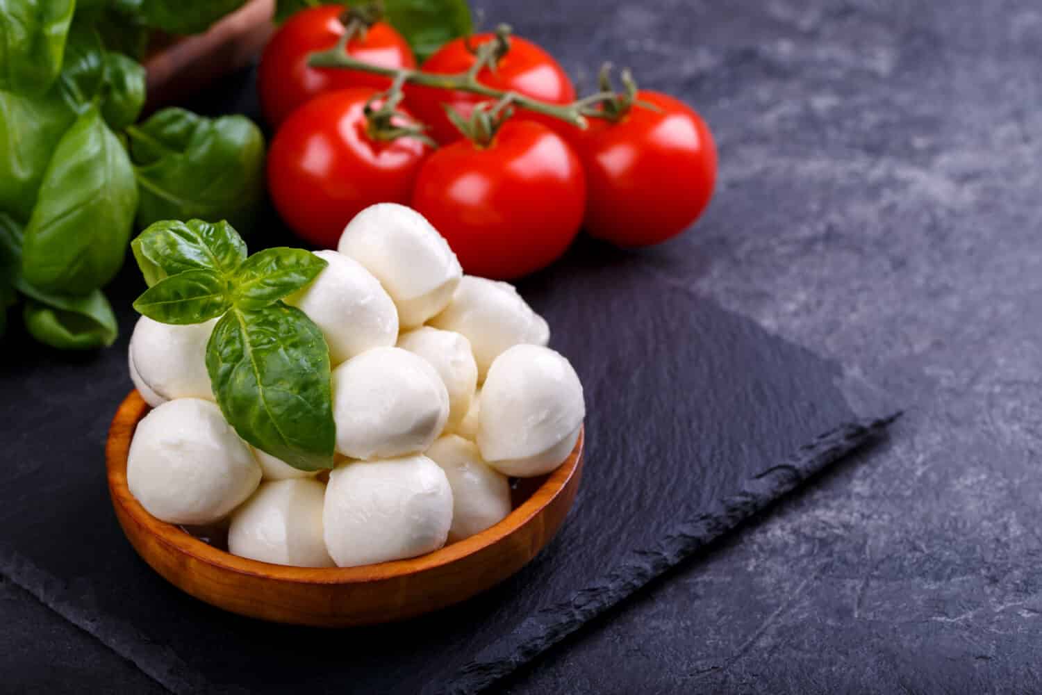 Mozzarella cheese, basil and tomato cherry on slate stone board, copy space. Ingredients for Caprese salad