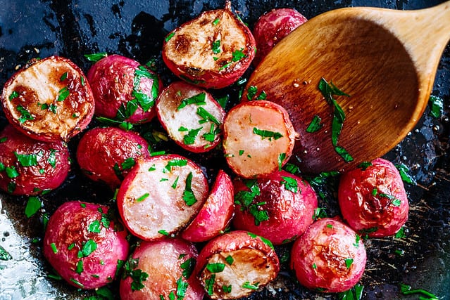 Beautiful roasted radishes in a pan with a wooden spoon close up