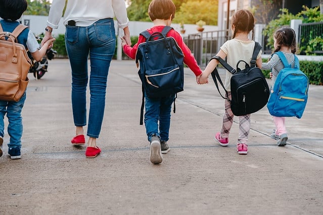 Mother and pupil and kids holding hands going to school in first class with schoolbag or satchel walking to school bus, Parent and son,sister preschool