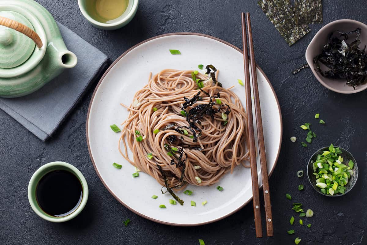Soba noodles with sauce and garnishes. Japanese food. Top view. Black slate background.