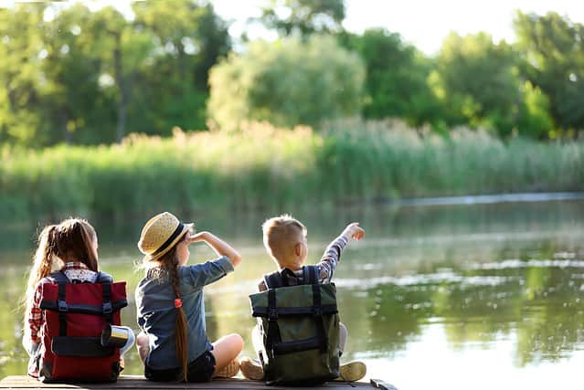 Little children sitting on wooden pier. Summer camp